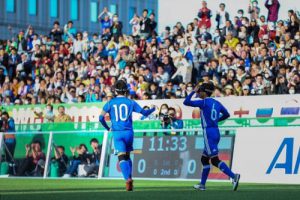 Japanese players run across the pitch watched by hundreds of fans