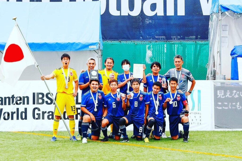 The Japanese men's blind football team pose with the Japanese flag for a group photo