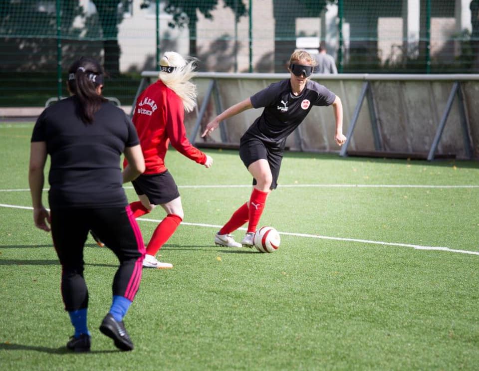 A female blind football player has possession of the ball, moving past a defender