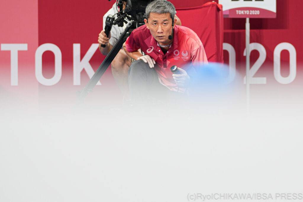 A goalball referee crouches and watches the ball closely during a game