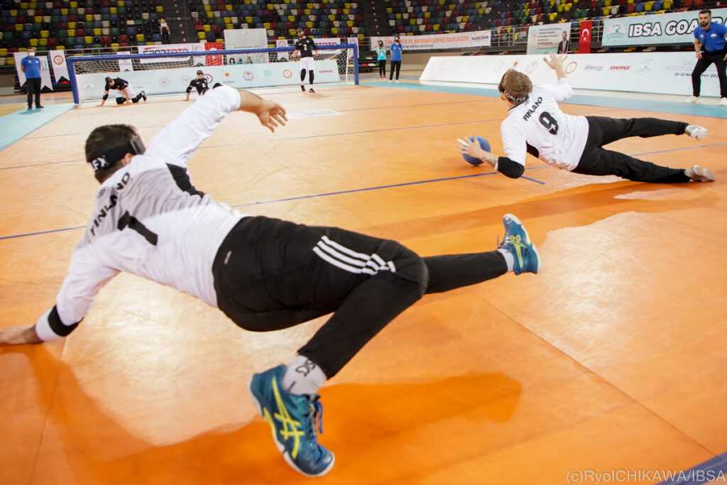 Two members of the Finnish men's goalball team extend their bodies during their defense of a shot